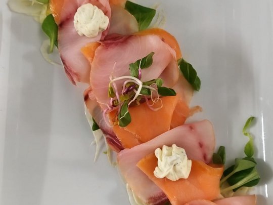 Restaurant Auf einem weißen Teller angerichtete Scheiben von Fisch und Gemüse mit Dips.