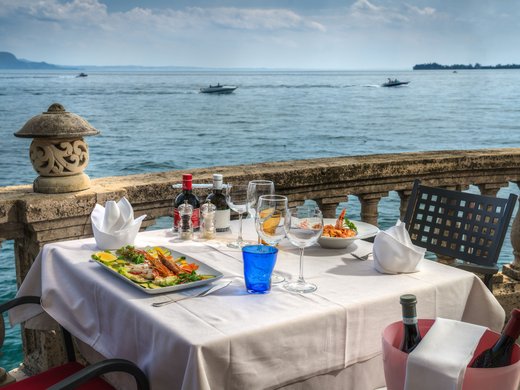 Willkommen in Eurem Hotel in Gardone Riviera! Eingedeckter Tisch mit Meeresblick und Meeresfrüchtegerichten