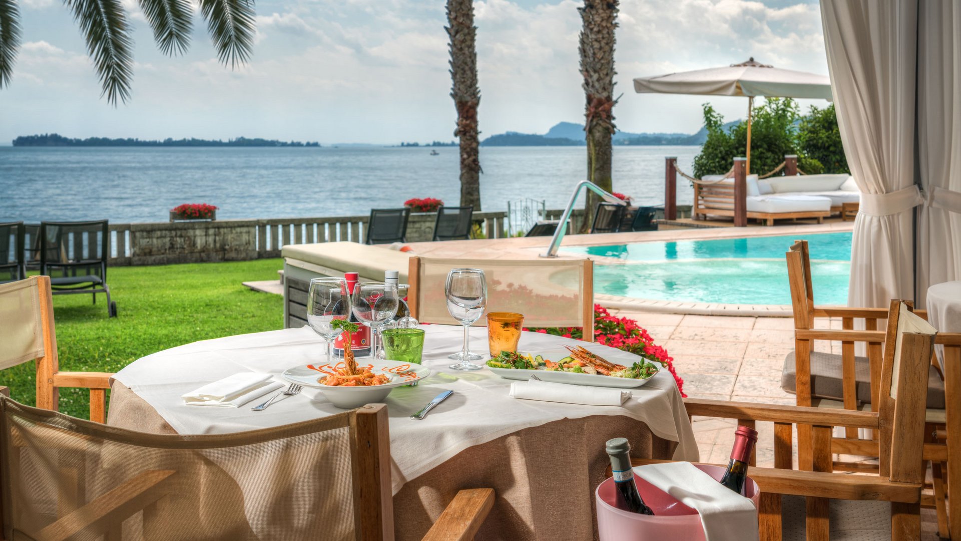 Restaurant Tisch mit Essen und Wein neben Pool und See mit Palmen