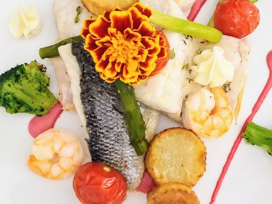 Restaurant Gourmetgericht mit Fisch, Garnelen, Gemüse und essbarer Blume auf weißem Teller