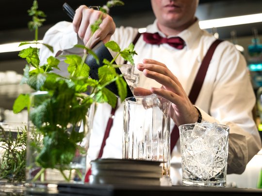 Lässiger Urlaub am Gardasee im 4-Sterne-Hotel Barkeeper füllt Eis in Mixer, frische Kräuter im Vordergrund