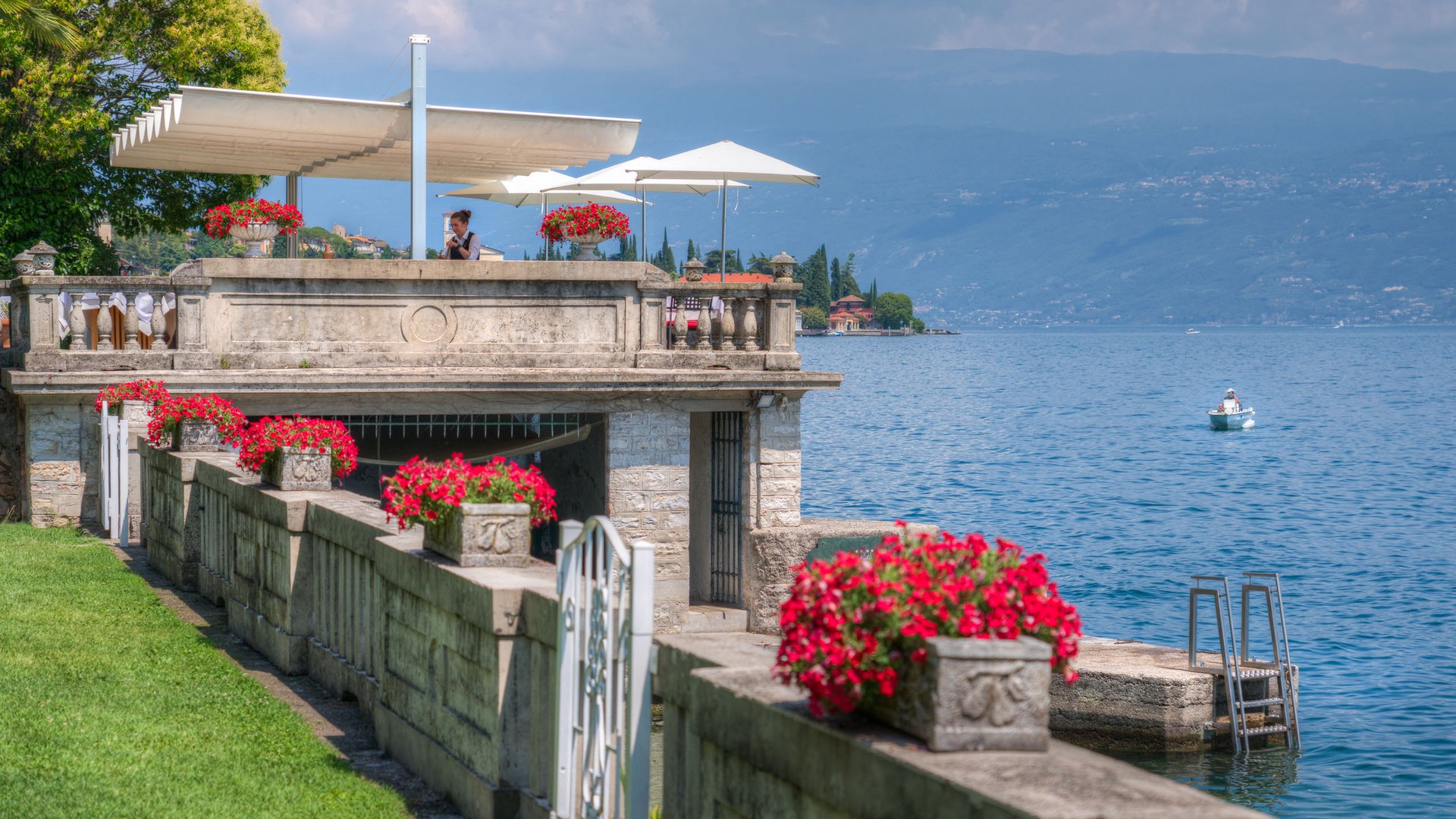 Restaurant Terrasse mit roten Blumen am See mit Bergen und Boot im Hintergrund