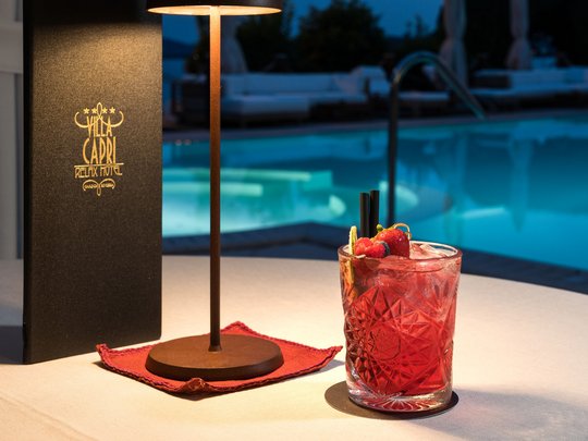 Leckeres in Eurem Hotel mit Strand am Gardasee Rotes Cocktailglas mit Früchten neben einer Lampe am Pool im Hotel Villa Capri
