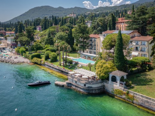 Willkommen in Eurem Hotel in Gardone Riviera! Uferpromenade mit Boot, Schwimmbad und bewaldetem Hügel im Hintergrund