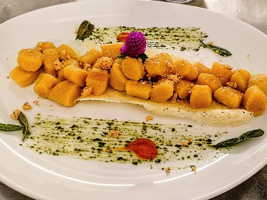Restaurant Kürbisgnocchi auf Parmesanchip mit Kräutern und Blume angerichtet